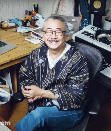 Nobuo Uematsu : la pudeur d’un compositeur qui a marqué des générations Nobuo Uematsu sourit au milieu de son matériel de création, entouré d’un ordinateur, d’un clavier et de son espace de travail.