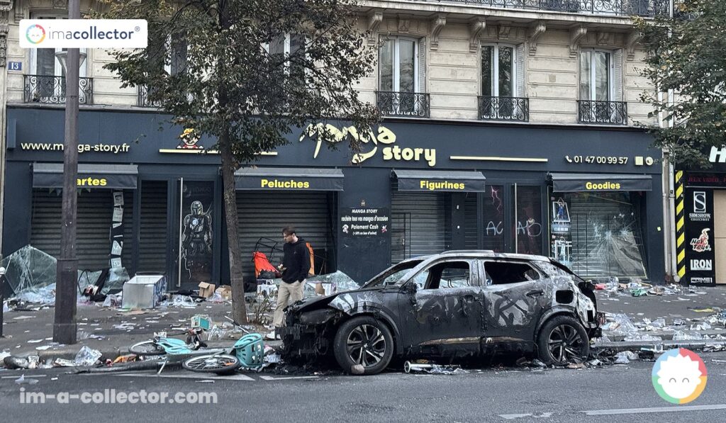 Façade du magasin Manga Story à Paris, aux vitrines endommagées, avec une voiture incendiée et des débris jonchant la chaussée.